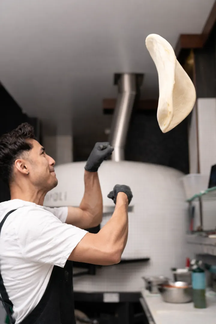 Pizzaiolo tossing dough in front of the wood-fired oven
