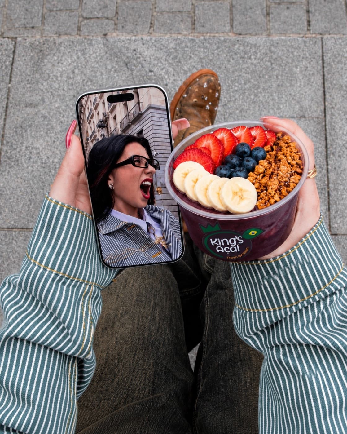 A hand holding up a phone beside an acai bowl